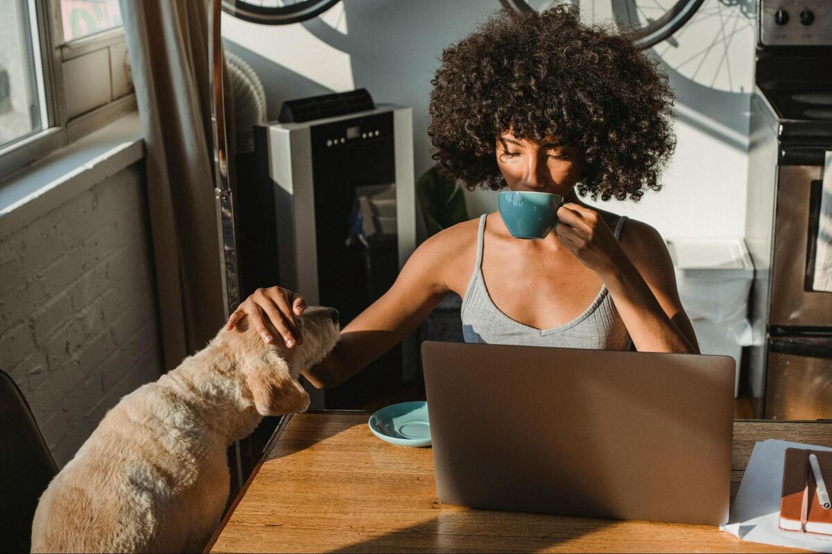 Woman working from home with coffee in hand while petting her dog