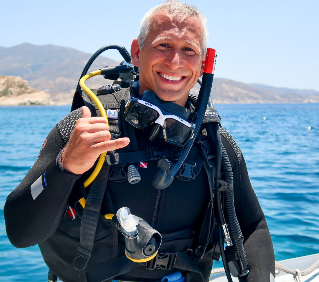 Man in scuba diving gear giving a hand signal on an inflatable boat.