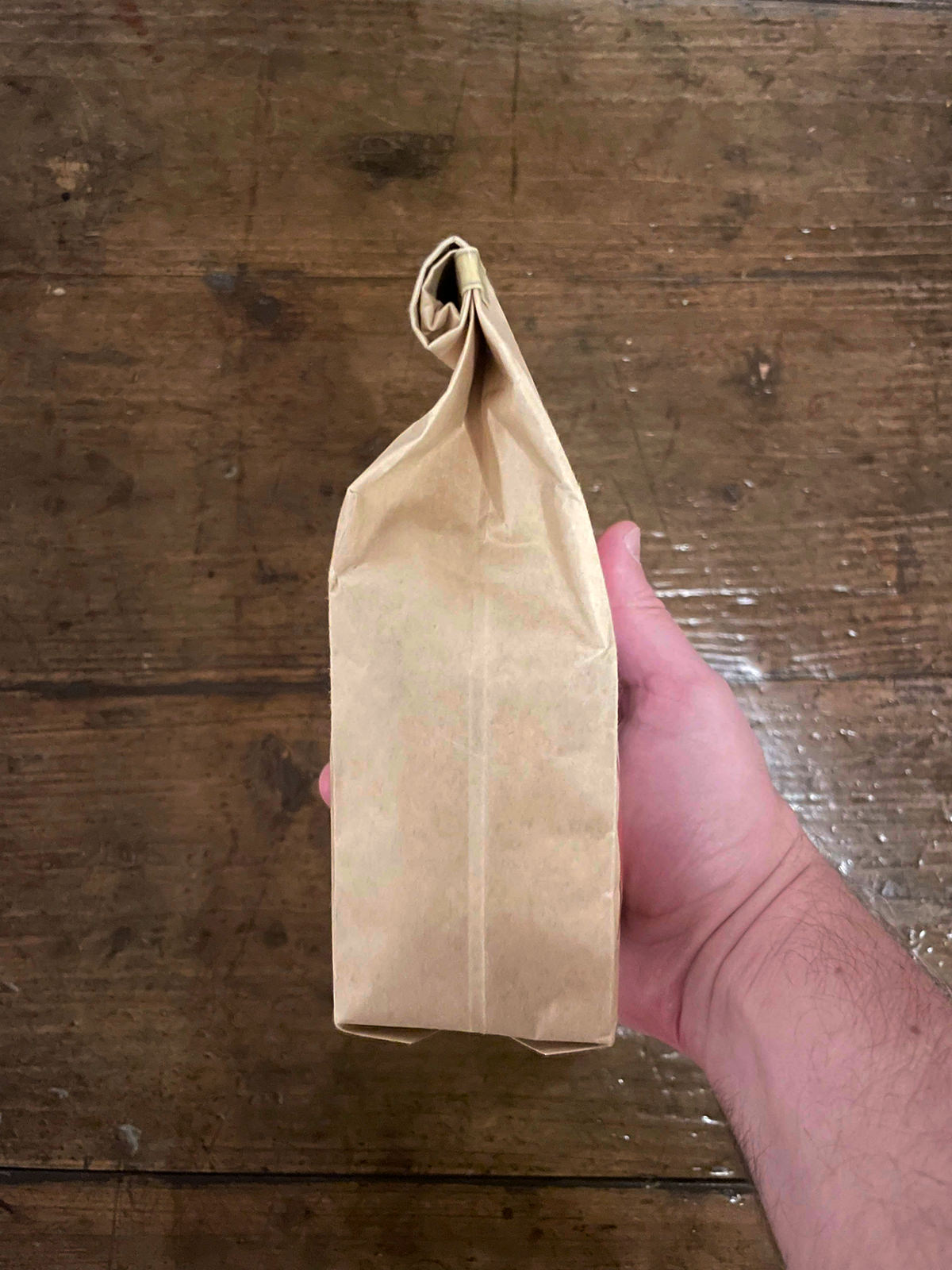 Hand holding a kraft coffee bag against a wooden background