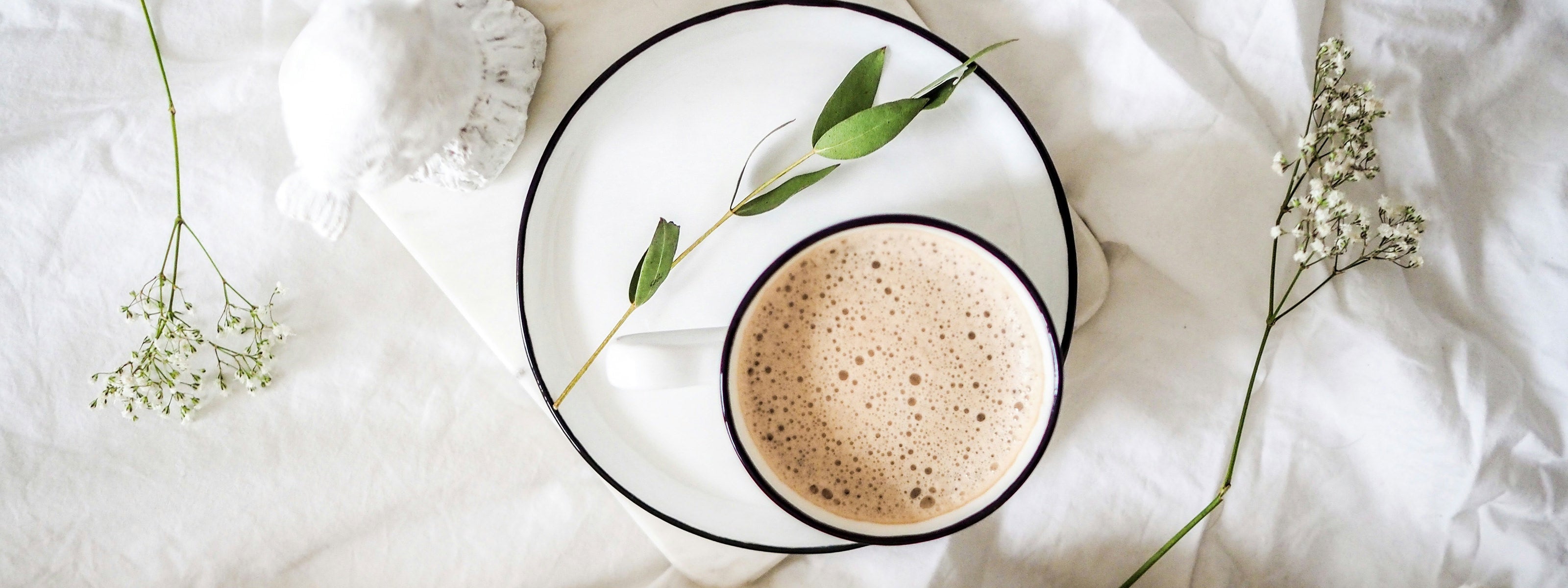 Cup of coffee on a white plate with green leaves on a light fabric background