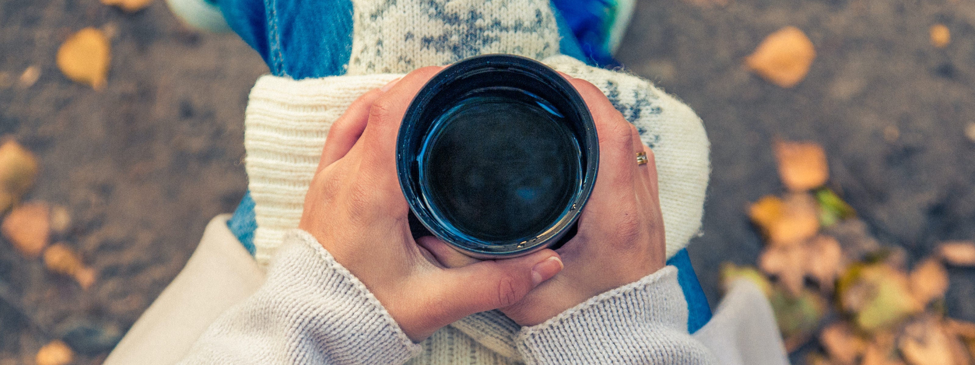 looking down at at pair of female hands holding a cup of coffee in an outdoor setting.